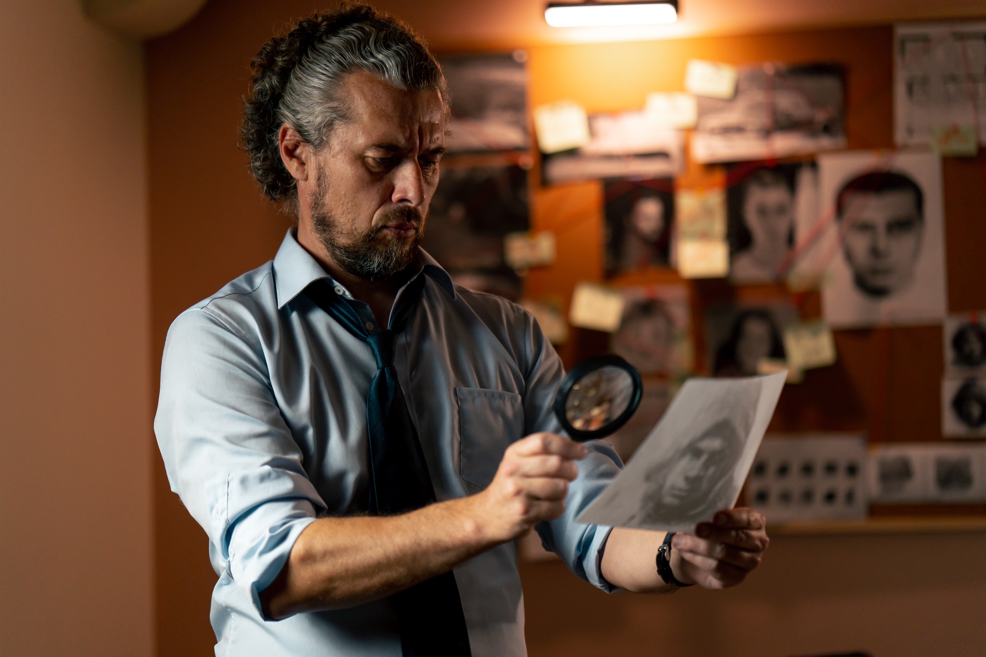 in the detective's office middle-aged investigator in a shirt and tie examines with a magnifying