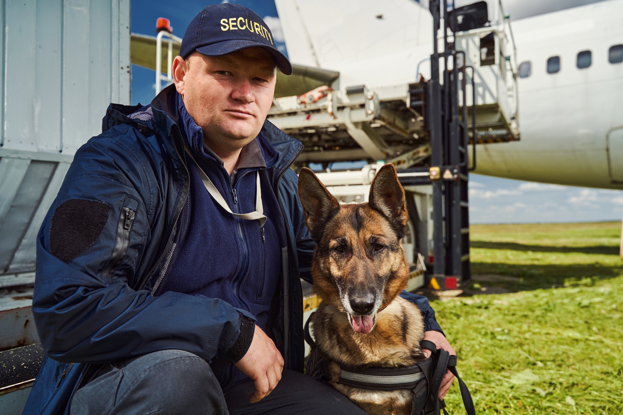 Male security guard hugging dog at airfield