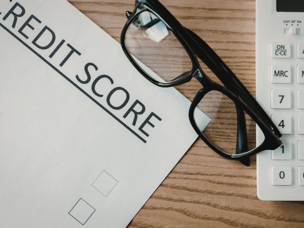 A credit score document, essential for background screening, sits next to black eyeglasses and a white calculator on a wooden desk.