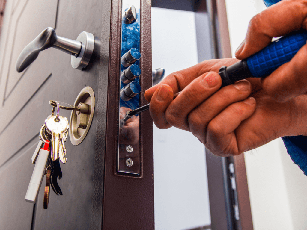 A person uses a screwdriver to install or repair a door lock, with keys hanging from the lock—a simple step in vacation home security for peace of mind while enjoying summer travel.