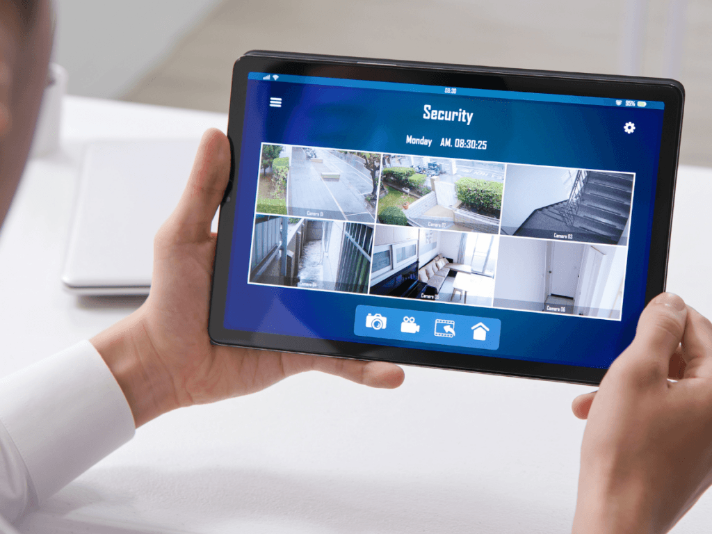Person holding a tablet displaying a security camera monitoring app with live feeds from multiple locations, ideal for keeping an eye on your property and ensuring vacation home security during summer travel.